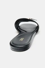 Sandalia plana color crudo con detalle de tira con hebilla dorada en la parte delantera.