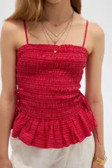 Top de algodón con diseño estampado de cuadros vichy en tonos celeste y blanco, corte al cuerpo con escote recto y tirantes finos. Presenta cuerpo fruncido tipo smock con cordones ajustables en los laterales que forman un pequeño volado en el ruedo.