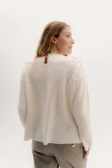 Buzo de lambswool color beige, con escote redondo y detalle en V. Presenta cierres metálicos en los puños que revelan un interior en contraste de color marrón y ribete rojo. Tiene tajos laterales para mayor comodidad y un fit amplio.