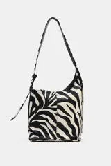 Bolso mini tipo saca asimétrica confeccionado en piel con pelo y estampado animal de cebra. Tiene asa de hombro ajustable, bolsillo interior con cremallera y cierre mediante imán.