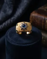 Anillo ancho de bronce con baño de oro, diseño texturizado, estrella central decorada con circonias y piedra azul, y pequeñas piedras verdes en los laterales.