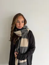 Bufanda de tejido suave con diseño de cuadros grandes en tonos negro y beige, terminada con flecos en los extremos.