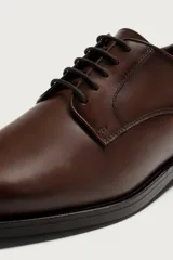 Zapato de vestir estilo Derby en piel color marrón oscuro, con cordones del mismo tono, horma redonda y suela con ligero tacón.