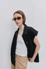 Chaleco de jean negro, de calce relajado con hombros caídos, cuello camisero, cierre frontal con botones y grandes bolsillos aplicados.