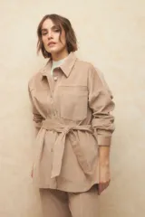 Sobrecamisa de pana color beige, con cuello camisero, cierre frontal con botones metálicos, mangas largas con puños abotonados y lazo ajustable en la cintura.
