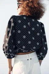 Blusa azul marino con estampado de lunares blancos, cuello redondo y mangas abullonadas. Presenta detalles de bordados perforados, volantes delanteros y acabados elásticos.