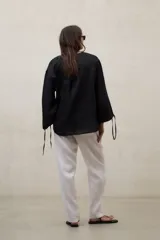 Blusa de lino blanca de corte amplio, con escote en V, mangas largas y puños con abertura y lazo.
