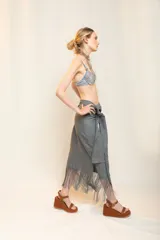 Falda midi color beige de tiro alto y silueta envolvente, con lazo ancho para anudar en la cintura, diseño asimétrico y terminación de flecos largos en el ruedo.