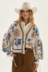 Cardigan de tejido de punto color crudo con diseño de jacquard floreado en tonos azules y marrones. Presenta cuello en V, cierre frontal con botones y ribetes a rayas en cuello, puños y bajo.