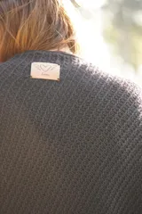 Poncho tejido en lana merino color marrón, con diseño de punto acanalado y terminación con flecos en el borde inferior. Incluye una pequeña etiqueta de cuero en la parte posterior.
