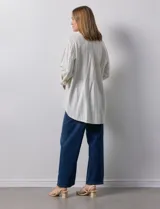 Camisa de lino a rayas verticales color crema, con cuello con solapa, abertura central con botones, bolsillos delanteros y mangas 3/4 regulables con presilla y botón.