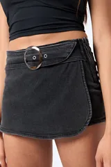 Minifalda tipo short pollera cruzada, color negro lavado, con cinturón integrado de denim y hebilla metálica redonda.