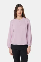 Blusa de manga larga con cuello redondo y cierre frontal parcial mediante botones forrados. Presenta diseño de doble capa en el frente y puños abotonados.