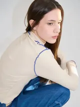 Polera de cuello alto confeccionada en tela rib color blanco, con mangas largas y hombreras. Presenta pespuntes en contraste en las terminaciones del cuello, hombros y puños.