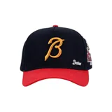 Gorra tipo baseball con visera roja y cuerpo azul marino. Presenta una letra B bordada en color dorado en el frente, la palabra Desires bordada en blanco y un parche lateral con diseño gráfico.