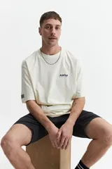 Remera de manga corta color crema, corte oversize, con cuello redondo y estampado con texto y diseño floral en el frente.