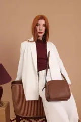 Bandolera de diseño compacto en color beige, confeccionada en material símil cuero con textura granulada. Cuenta con un bolsillo frontal con cierre y correa larga regulable.