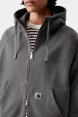 Campera con capucha de corte holgado, color gris oscuro efecto desgastado, con cierre frontal completo, cuello alto, bolsillos tipo canguro y mangas raglán. Presenta una pequeña etiqueta cuadrada con el logo de la marca en el bolsillo izquierdo.