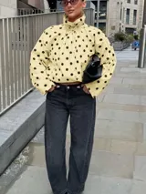 Chaqueta ligera de color amarillo con estampado de lunares negros, cuello alto, mangas largas anchas y cordón ajustable en el dobladillo inferior.