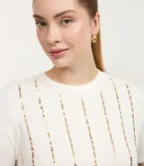 Remera de viscolycra color crudo, de corte regular, con cuello redondo, mangas cortas y apliques de lentejuelas verticales.