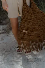 Bolso de mano grande tejido a crochet con técnica de trapillo reciclado, color beige visón. Presenta un diseño de punto grueso y flecos largos en el borde inferior.