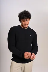 Sweater de punto con textura acanalada, color negro, de cuello redondo y manga larga. Presenta un pequeño logo bordado en el pecho.
