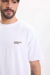 Remera blanca de manga corta con estampa en la espalda dividida en cuatro paneles de temática surfera con la inscripción "Sunshine Waves".