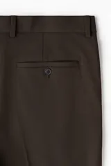 Pantalón de vestir color marrón oscuro, corte slim fit, con pliegue marcado en la pierna y puños doblados. Presenta cierre frontal con botón y bolsillos laterales y traseros.