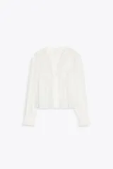 Blusa blanca de manga larga con escote en pico y cuello redondo. Cuenta con bordados florales frontales a tono, puños con volados y cierre frontal de botones.