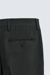 Pantalón de vestir negro con pliegues frontales, corte regular fit, bolsillos laterales y traseros de doble vivo con botón. Cierre frontal cruzado con cremallera y gancho metálico.