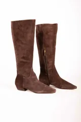 Bota de caña alta confeccionada en gamuza color marrón, con diseño de punta cuadrada y taco bajo cuadrado. Presenta cierre lateral interno y una estructura minimalista.