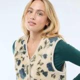 Chaleco sin mangas confeccionado en tejido tipo corderito, con estampado floral en tonos azules y verdes sobre base beige. Presenta escote en V, cierre frontal con botones a presión y ribetes en color crema.