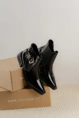 Botín negro de charol con punta cuadrada y hebilla metálica decorativa.