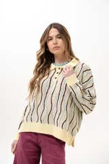 Buzo de punto tipo polo en tono amarillo claro con diseño de ondas a rayas en tonos marrón y celeste. Presenta cuello clásico, cierre frontal parcial con botones y silueta relajada con mangas largas.