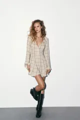 Vestido corto de algodón con estampado de cuadros en tonos beige y marrón. Presenta escote en pico, manga larga con corte evasé y bajo con volantes. Incluye cierre frontal con ganchos metálicos y cremallera lateral oculta.