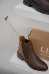 Botinetas de cuero color marrón con diseño tipo chelsea, con paneles laterales elásticos y detalle de cuero texturizado con acabado metalizado en el talón. Poseen taco bajo cuadrado y terminación redondeada.