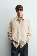 Camisa de algodón de corte relajado, color beige con finas rayas verticales en tonos gris y amarillo. Presenta cuello solapa, manga larga con puños abotonados y bajo con aberturas laterales.