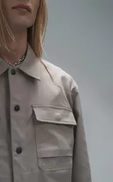 Chaqueta de corte regular crop confeccionada en microfibra pesada levemente elastizada. Presenta cuello volcado, cierre frontal con broches snap a tono y bolsillos delanteros con solapa.