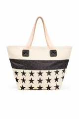Bolso tipo tote de material textil con textura rústica, color beige con estampado de estrellas negras y una franja horizontal de glitter negro. Cuenta con asas largas de color claro y detalles de parches cuadrados negros en la unión de las asas.