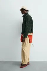 Cazadora regular fit de piel con acabado en ante color verde oscuro, de la colección especial Gabriel Azevedo x ZARA. Cuenta con cuello subido, manga larga, bolsillos de vivo en la cadera, bolsillo interior y bajo acabado con elástico. Cierre frontal con cremallera oculta por solapa con botones a presión.