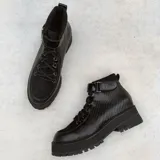Botas negras de caña baja con textura simil reptil, cordones, suela flatform dentada y tira con hebilla en el tobillo.