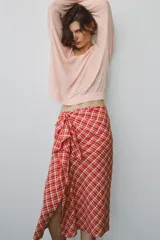 Falda midi de tiro medio ZARA WOMAN COLLECTION confeccionada en hilatura con algodón, con estampado de cuadros en tonos rojos y blancos. Presenta detalle de pliegue con lazadas en el delantero y bajo recto con abertura. Cierre con cremallera oculta en costura.