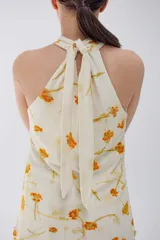 Minivestido color crema con estampado de flores amarillas, cuello halter y falda con volados.