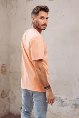 Remera color durazno de corte recto y manga corta, con cuello redondo y pequeño bordado de dos patos en el pecho.