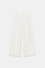 Pantalón wide leg de tiro medio, color blanco con diseño de rayas diplomáticas a contraste, bolsillos laterales y de vivo en la espalda, pinzas en el delantero y cierre frontal con cremallera, botón y ganchos metálicos.