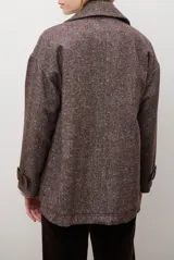 Chaquetón de lana color bordó con diseño de espiga y motas blancas. Tiene solapa, doble abotonadura frontal, mangas largas con detalle de correa y hebilla en los puños.