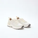 Zapatillas estilo running de color beige, confeccionadas con una combinación de paneles de cuero sintético y malla transpirable. Presentan cordones al tono, suela robusta con relieve y detalles en color marrón oscuro en la base.