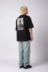 Remera de corte oversize confeccionada en algodón pesado, color negro. Presenta un bordado minimalista en el centro del pecho con forma de ojo y un parche estampado en la espalda que ilustra una mano abriendo una persiana.