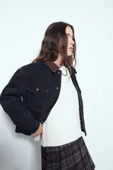 Campera de jean color negro con cuello de pana en tono marrón, cierre frontal con botones y bolsillos en el pecho. Presenta un diseño de corte relajado y ligeramente cropped, con interior forrado en corderito para mayor abrigo.