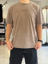 Remera oversize gris con efecto acid wash, de mangas cortas y cuello redondo, con estampado tipográfico blanco en la espalda.